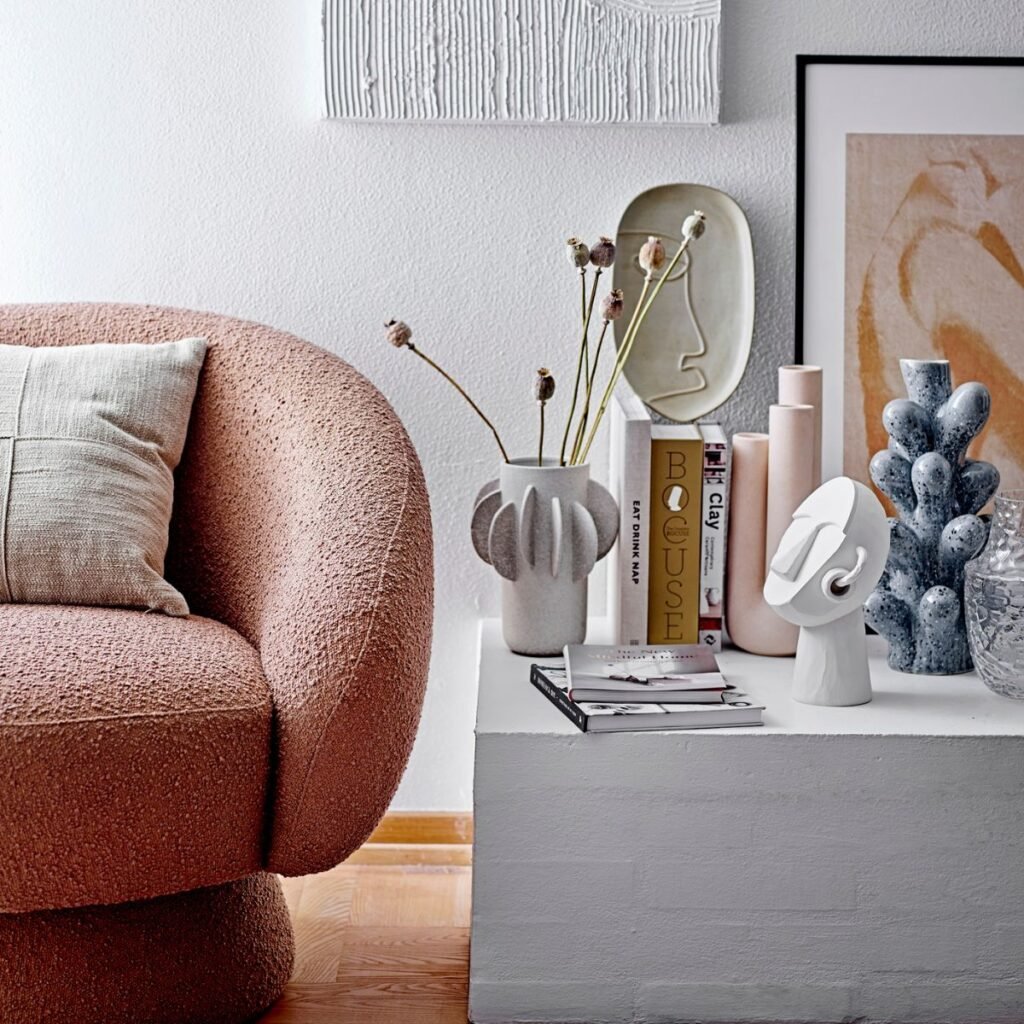  Gros plan sur un fauteuil en tissu bouclette terracotta, entouré d’objets décoratifs modernes aux formes organiques et aux couleurs douces.